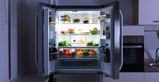 An open refrigerator door revealing shelves filled with various food items and drinks.