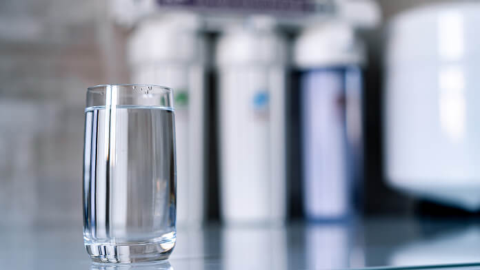 A glass of water on a counter beside a water filter, highlighting the importance of clean drinking water.